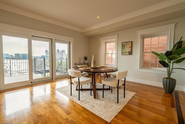 dining area featuring a city view, ornamental molding, light wood-type flooring, and baseboards