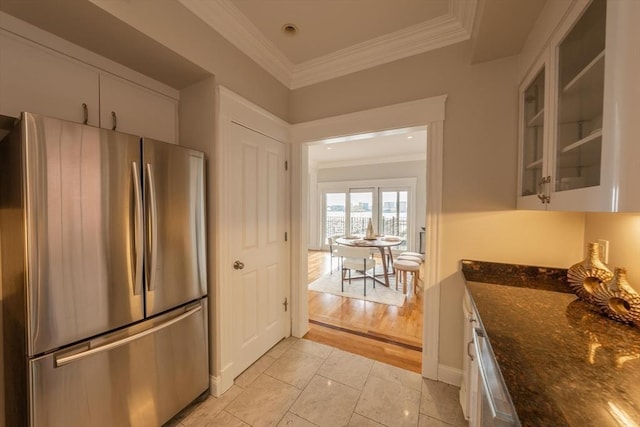 kitchen with glass insert cabinets, ornamental molding, dark stone counters, and freestanding refrigerator