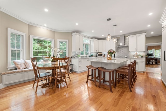 kitchen featuring wall chimney exhaust hood, crown molding, pendant lighting, light hardwood / wood-style floors, and white cabinetry