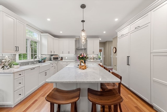 kitchen featuring light wood-type flooring, white cabinetry, a kitchen island, and sink