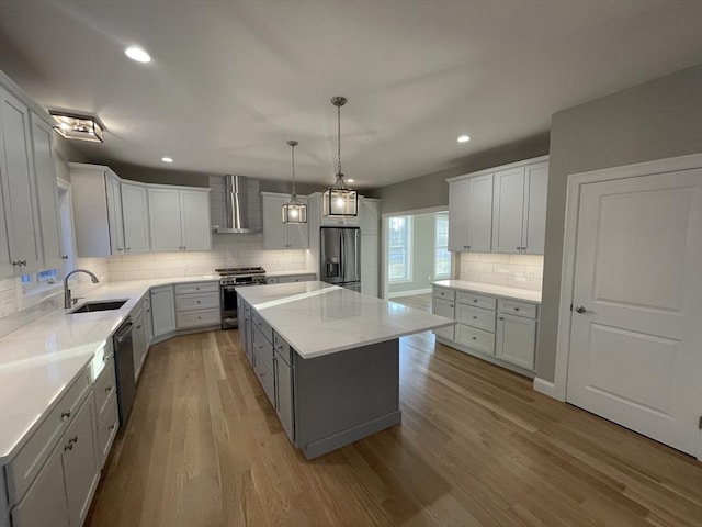 kitchen featuring appliances with stainless steel finishes, wall chimney exhaust hood, sink, light hardwood / wood-style flooring, and a kitchen island