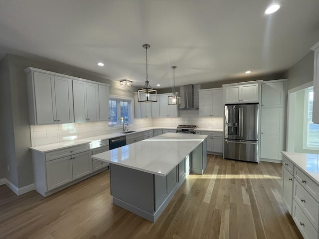 kitchen featuring a center island, wall chimney range hood, sink, light hardwood / wood-style flooring, and appliances with stainless steel finishes