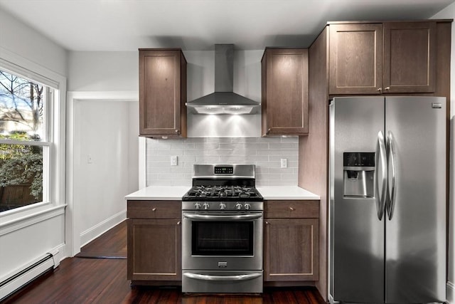 kitchen featuring appliances with stainless steel finishes, backsplash, a baseboard heating unit, dark wood-type flooring, and wall chimney exhaust hood