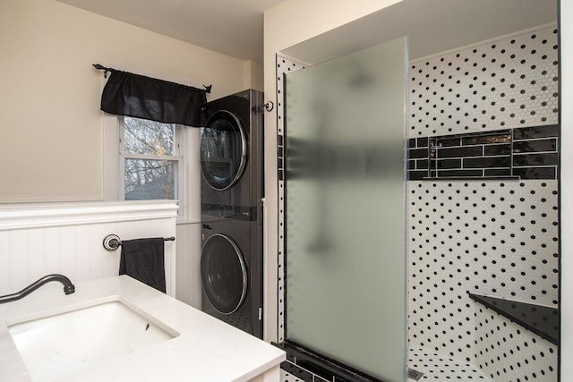 bathroom featuring stacked washer / dryer, wainscoting, a sink, and a shower stall