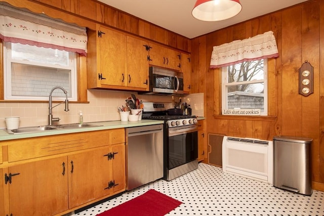 kitchen featuring heating unit, stainless steel appliances, light countertops, a sink, and wood walls