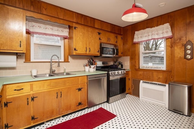 kitchen featuring wooden walls, appliances with stainless steel finishes, heating unit, light countertops, and a sink