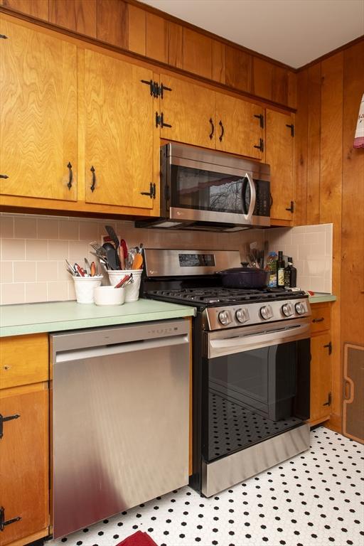 kitchen with wood walls, light countertops, appliances with stainless steel finishes, brown cabinets, and tasteful backsplash