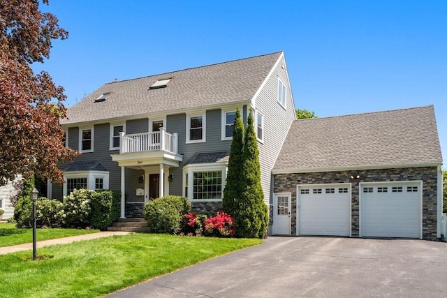 view of front of house with asphalt driveway, a balcony, an attached garage, roof with shingles, and a front lawn
