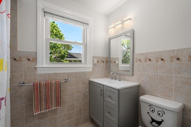 full bath featuring tile walls, toilet, vanity, and a wainscoted wall