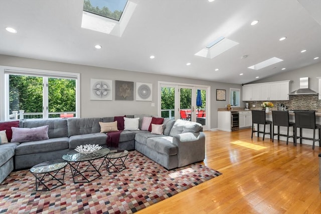 living area featuring a skylight, wine cooler, vaulted ceiling, plenty of natural light, and light wood-style flooring