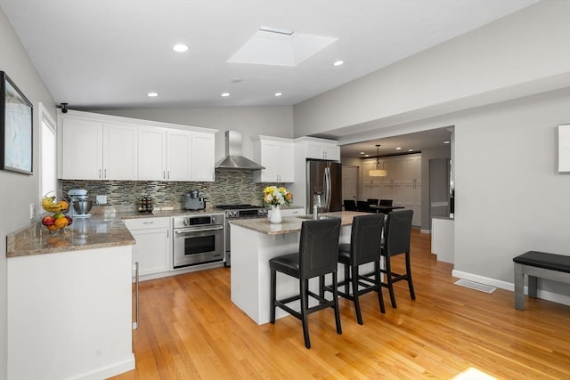 kitchen with stainless steel appliances, vaulted ceiling, wall chimney range hood, backsplash, and white cabinets