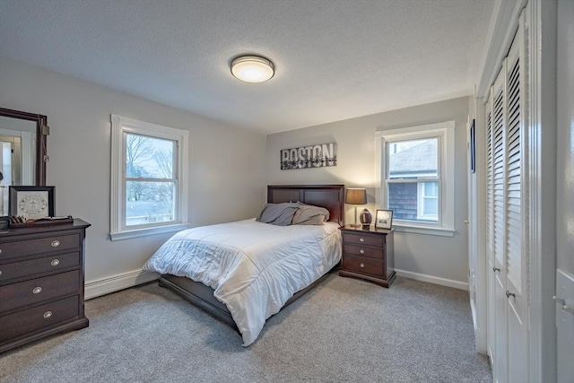 bedroom with light carpet, a textured ceiling, multiple windows, and a baseboard heating unit