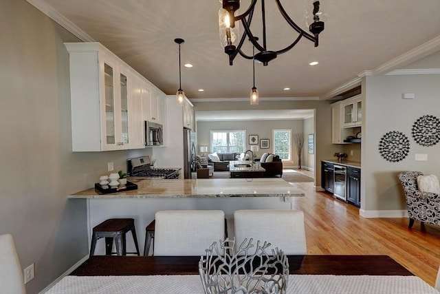 kitchen featuring pendant lighting, appliances with stainless steel finishes, white cabinets, a kitchen bar, and kitchen peninsula