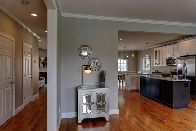 kitchen featuring a kitchen island with sink, hanging light fixtures, ornamental molding, and appliances with stainless steel finishes