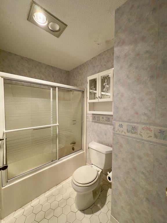 bathroom with a textured ceiling, bath / shower combo with glass door, tile patterned floors, and toilet