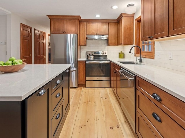 kitchen featuring brown cabinetry, decorative backsplash, under cabinet range hood, a sink, and stainless steel appliances