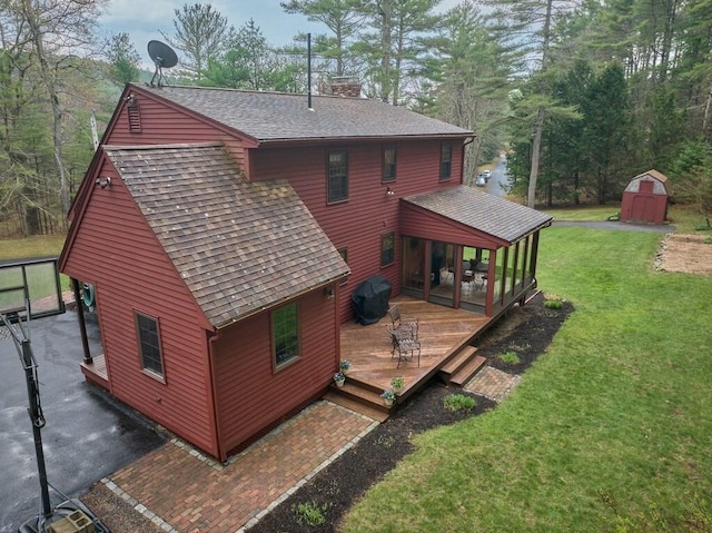 back of property with a wooden deck, a chimney, a storage unit, a lawn, and an outbuilding