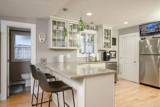 kitchen featuring hanging light fixtures, stainless steel appliances, a baseboard radiator, a kitchen breakfast bar, and kitchen peninsula