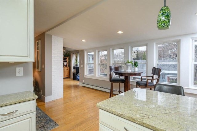 kitchen featuring pendant lighting, light wood-type flooring, baseboard heating, light stone counters, and white cabinetry