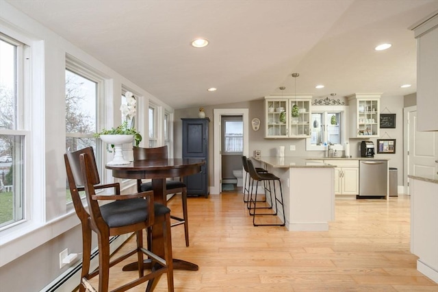 kitchen with pendant lighting, white cabinets, vaulted ceiling, stainless steel dishwasher, and a baseboard radiator