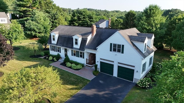 view of front of property featuring aphalt driveway, a garage, a chimney, a front yard, and a view of trees