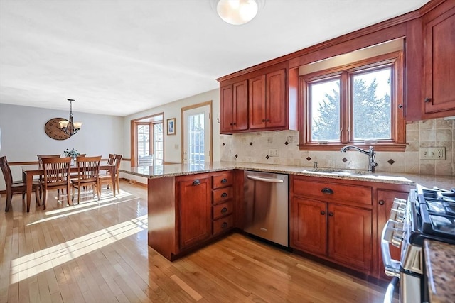 kitchen featuring light stone counters, a peninsula, a sink, appliances with stainless steel finishes, and light wood-type flooring