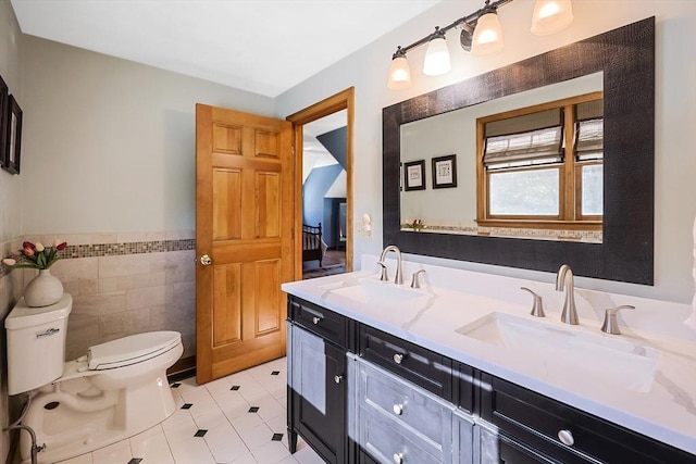 full bathroom with double vanity, a sink, toilet, and tile walls