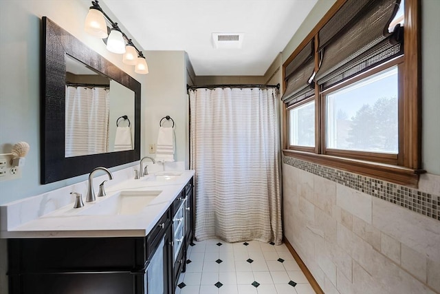 full bathroom with double vanity, tile walls, visible vents, and a sink