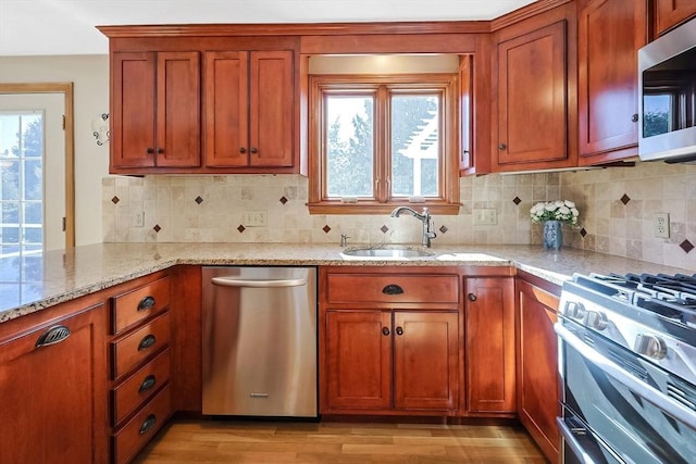 kitchen featuring light stone counters, a sink, appliances with stainless steel finishes, decorative backsplash, and light wood finished floors