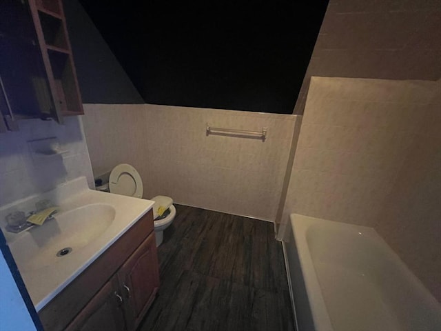 bathroom featuring vanity, wood-type flooring, tile walls, toilet, and a tub