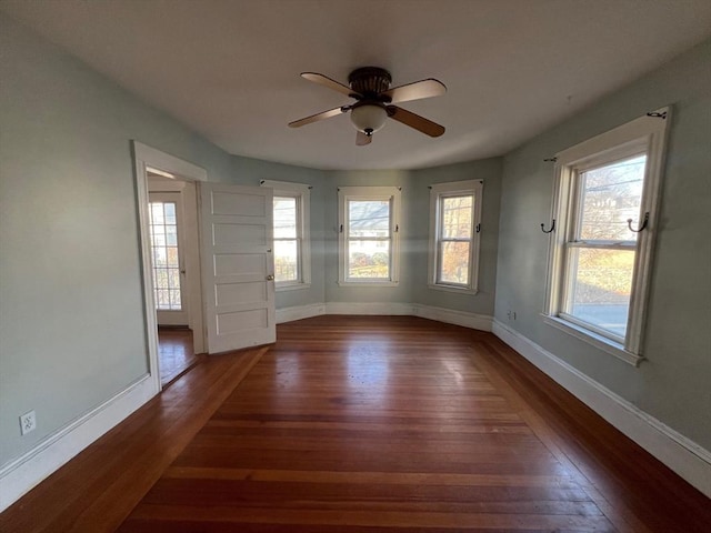 unfurnished room featuring a healthy amount of sunlight, ceiling fan, and dark wood-type flooring