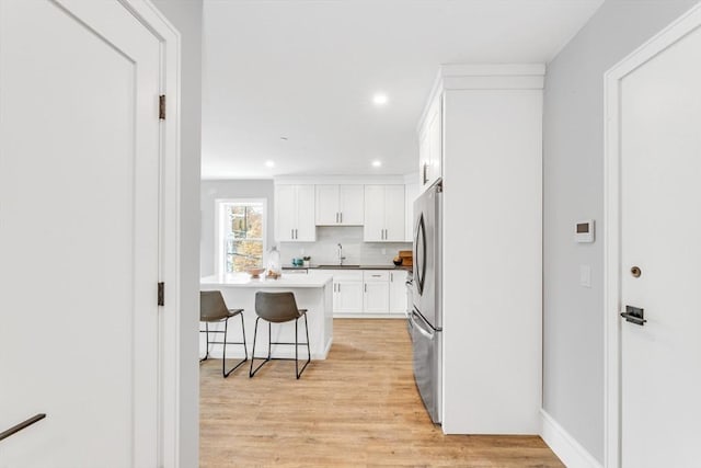 kitchen with light wood-style flooring, a kitchen bar, a sink, freestanding refrigerator, and white cabinets