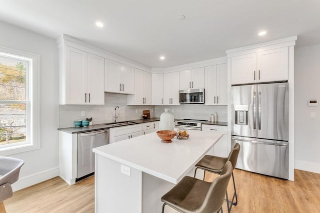 kitchen featuring light wood finished floors, stainless steel appliances, baseboards, and a sink