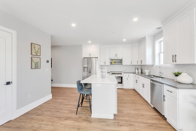 kitchen featuring a sink, a kitchen breakfast bar, baseboards, appliances with stainless steel finishes, and decorative backsplash