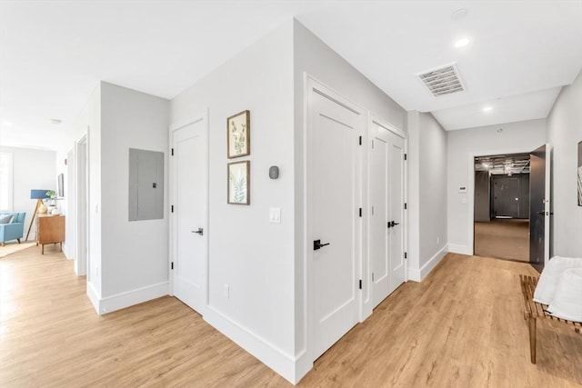 corridor with electric panel, light wood-style floors, visible vents, and baseboards
