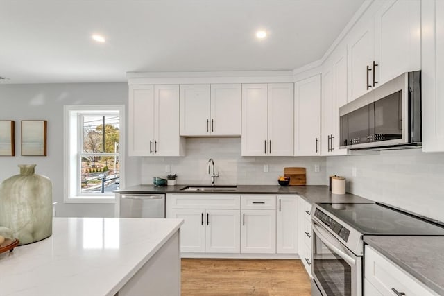 kitchen featuring light wood finished floors, appliances with stainless steel finishes, white cabinets, and a sink