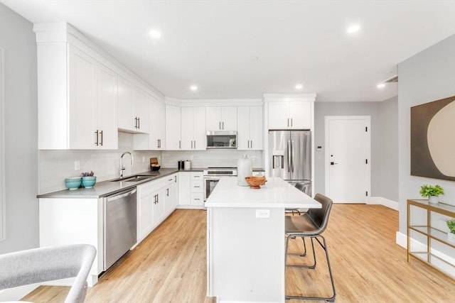 kitchen with a breakfast bar, a sink, white cabinetry, a kitchen island, and appliances with stainless steel finishes