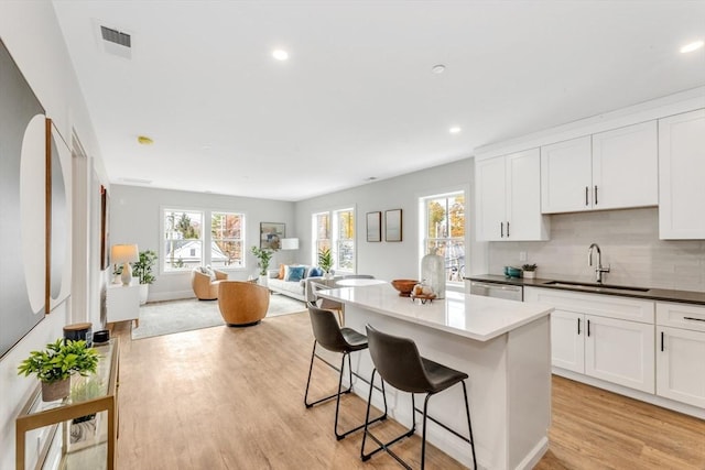 kitchen featuring light wood-style flooring, a center island, a breakfast bar, a healthy amount of sunlight, and a sink