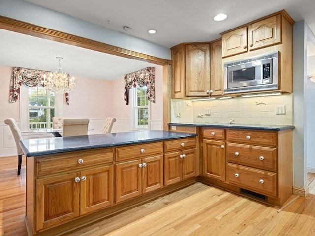 kitchen featuring plenty of natural light, stainless steel microwave, light hardwood / wood-style flooring, and tasteful backsplash