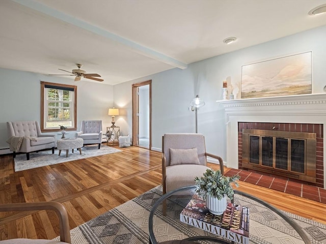 living room with a brick fireplace, wood-type flooring, and ceiling fan