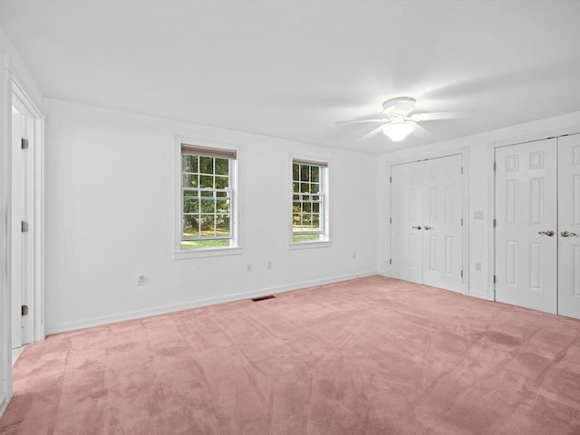 unfurnished bedroom with light carpet, ceiling fan, and two closets