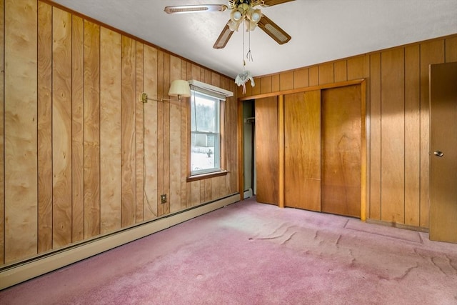 unfurnished bedroom featuring wooden walls, a baseboard heating unit, light colored carpet, ceiling fan, and a closet