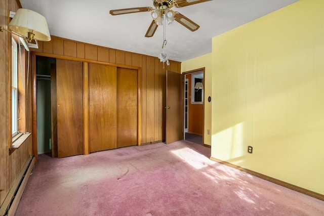 unfurnished bedroom featuring light carpet, baseboard heating, wooden walls, a closet, and ceiling fan