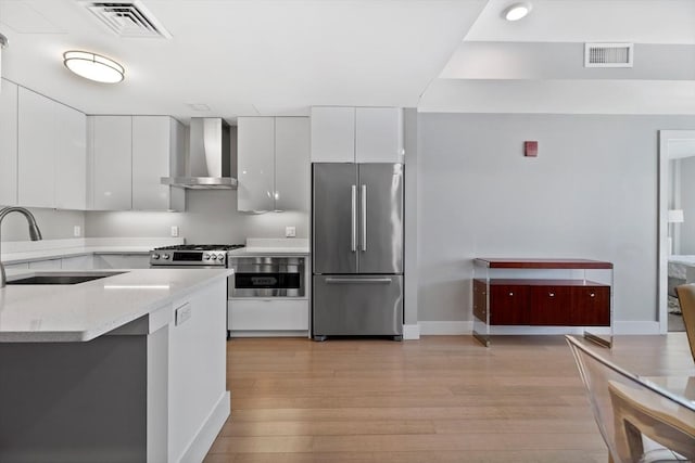 kitchen featuring stainless steel refrigerator, sink, white cabinets, light hardwood / wood-style floors, and wall chimney range hood