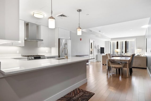 kitchen with decorative light fixtures, white cabinetry, stainless steel fridge, range, and wall chimney exhaust hood