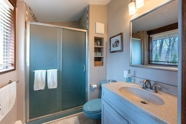 bathroom with toilet, a stall shower, built in shelves, and vanity