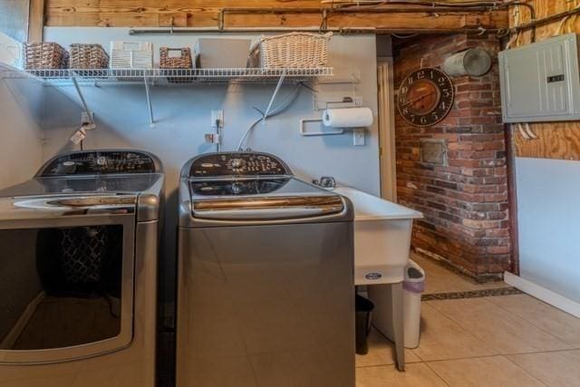 clothes washing area with washer and clothes dryer, light tile patterned floors, electric panel, and laundry area