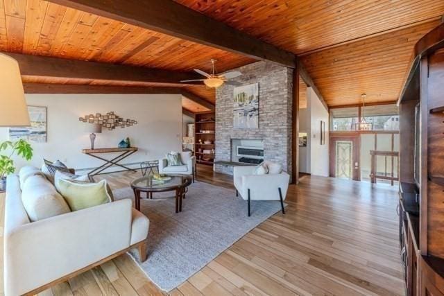 living room with wooden ceiling, wood finished floors, vaulted ceiling with beams, a fireplace, and a ceiling fan