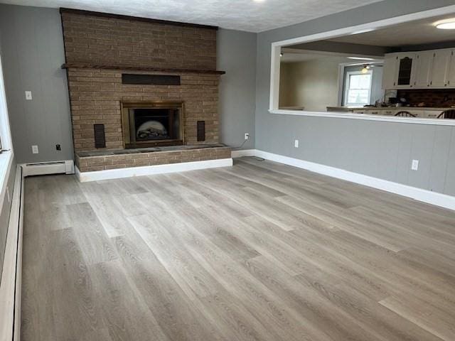 unfurnished living room with light wood-style floors, a brick fireplace, baseboards, and baseboard heating