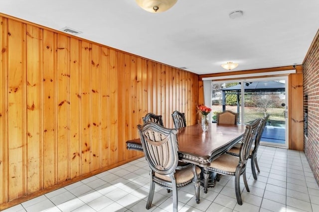 dining area featuring light tile patterned floors, brick wall, crown molding, and wood walls